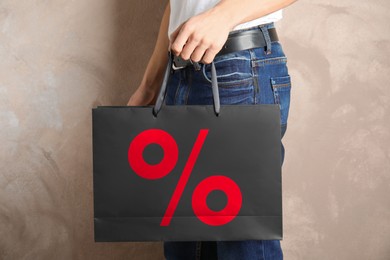 Man holding paper shopping bag with percent sign near beige wall, closeup. Discount concept