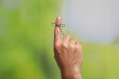 Photo of Man showing index finger with tied bow as reminder on green blurred background, closeup