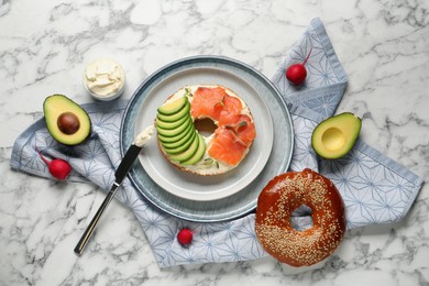 Delicious bagel with cream cheese, salmon and avocado on white marble table, flat lay