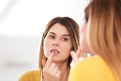 Woman applying cold sore cream on lips in front of mirror