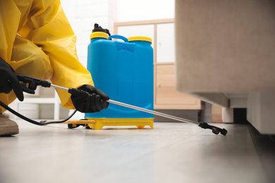 Pest control worker spraying pesticide under furniture indoors, closeup