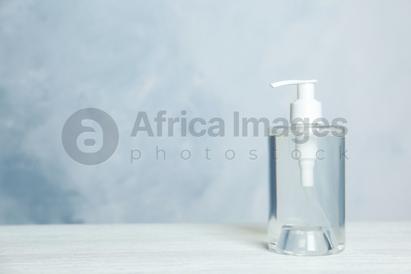 Dispenser bottle with antiseptic gel on table against light background. Space for text