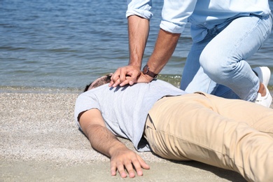 Passerby performing CPR on unconscious young man near sea. First aid