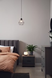 Photo of Stylish bedroom interior with comfortable bed, nightstand and green houseplant