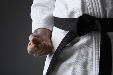Karate coach wearing kimono and black belt on grey background, closeup