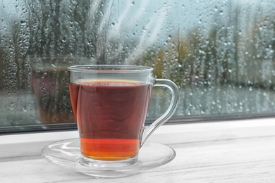 Glass cup of tea on windowsill. Rainy weather