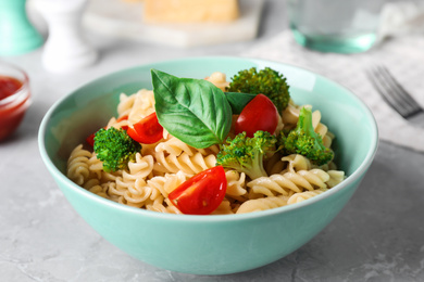 Tasty pasta with broccoli, cherry tomatoes and basil on light grey marble table, closeup