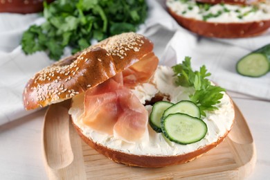 Delicious bagel with cream cheese, jamon, cucumber and parsley on wooden board, closeup