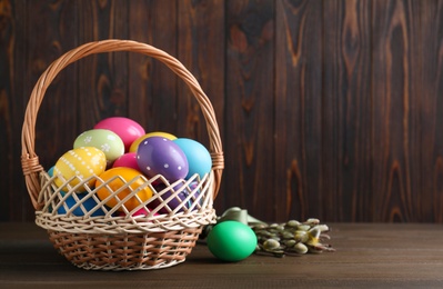 Colorful Easter eggs in wicker basket and willow branches on wooden background. Space for text
