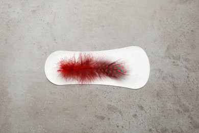 Sanitary pad with red feather on grey background, top view. Menstrual cycle
