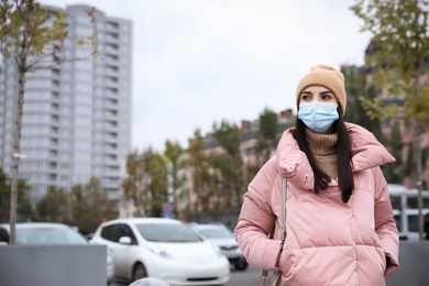 Young woman in medical face mask walking outdoors. Personal protection during COVID-19 pandemic