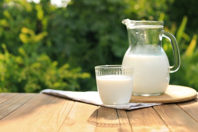 Glass and jug of tasty fresh milk on wooden table outdoors, space for text