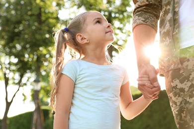 Father in military uniform walking with his daughter at sunny park