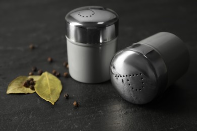 Photo of Salt and pepper shakers with bay leaves on black table, closeup