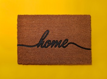 Photo of Doormat with word Home on yellow background, top view