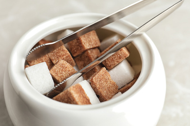 Different refined sugar cubes in bowl on light table, closeup
