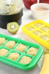 Banana and kiwi purees in ice cube tray with different fresh fruits white wooden table