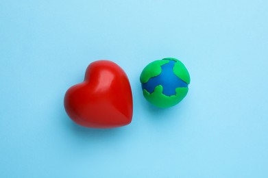 Plasticine model of planet and red heart on light blue background, flat lay. Earth Day