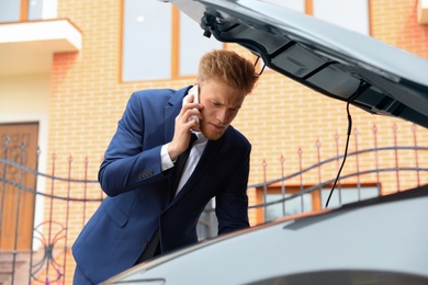 troubled young businessman talking on phone near broken car outdoors
