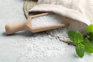Wooden scoop with natural sea salt, sack and mint on light grey marble table, closeup
