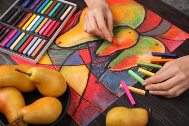 Woman drawing pears on paper with soft pastels at wooden table, closeup