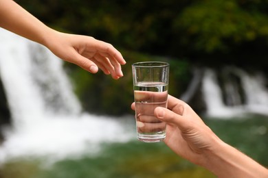 Man giving woman glass of fresh water near waterfall, closeup