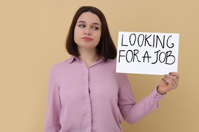 Photo of Young unemployed woman holding sign with phrase Looking For A Job on beige background