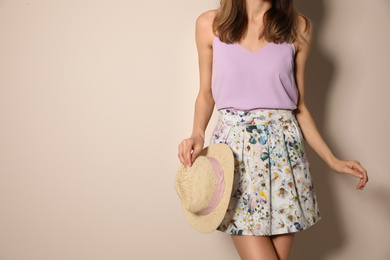 Young woman wearing floral print skirt with straw hat on beige background, closeup. Space for text