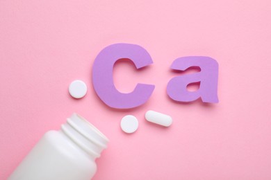 Pills, open bottle and calcium symbol made of purple letters on pink background, flat lay