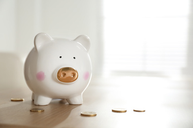 Piggy bank and coins on wooden table indoors. Space for text