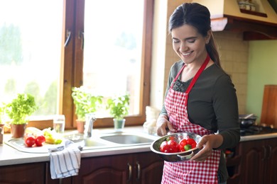 Young woman holding colander with fresh bell peppers in kitchen, space for text