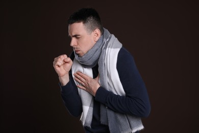 Young man with scarf coughing on dark background. Cold symptoms