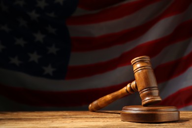 Judge's gavel on wooden table against American flag in darkness, space for text