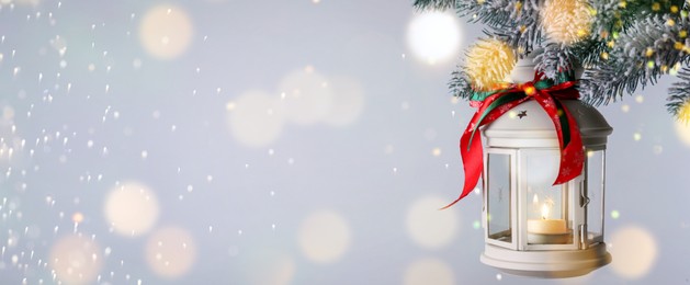 Image of Christmas lantern with candle hanging on snowy fir tree branch against light background, space for text. Banner design