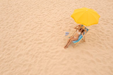 Woman resting in sunbed under yellow beach umbrella at sandy coast, space for text