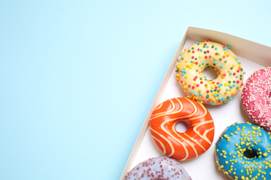 Delicious glazed donuts on light blue background, top view. Space for text