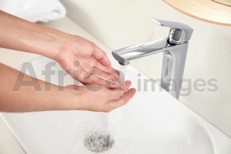 Young woman washing hands over sink in bathroom, closeup