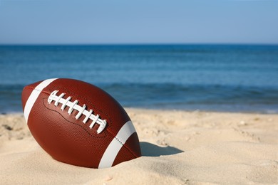 American football ball on beach. Space for text