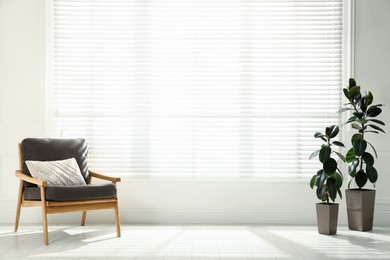 Photo of Comfortable armchair with pillow and plants near big window in spacious room. Interior design