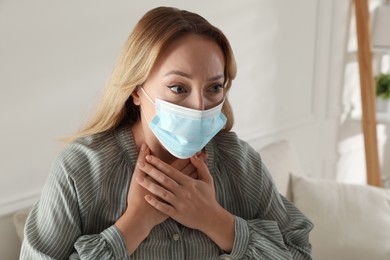 Young woman in medical mask suffering from pain during breathing at home