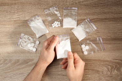 Man packing drugs in plastic bags at wooden table, top view