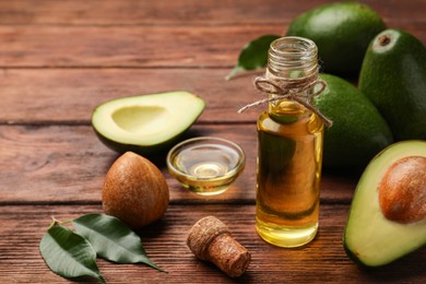 Photo of Glass bottle of cooking oil and fresh avocados on wooden table, closeup