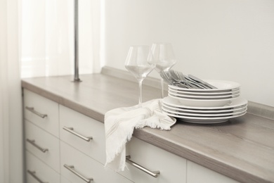 Clean dishware, cutlery and wineglasses on chest of drawers indoors
