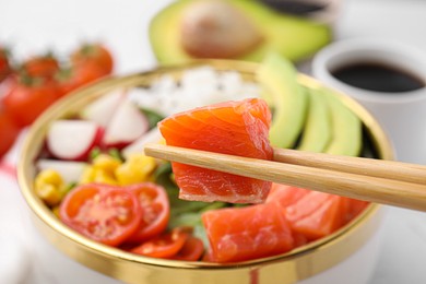 Photo of Chopsticks with salmon over delicious poke bowl, closeup
