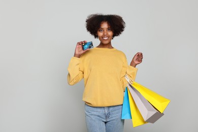Photo of Happy African American woman with shopping bags and credit card on light grey background
