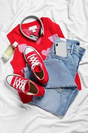 Photo of Pair of stylish red shoes, clothes and smartphone on white fabric, flat lay