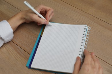 Left-handed woman writing in notebook at wooden table, closeup
