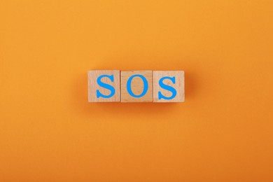 Abbreviation SOS made of wooden cubes on orange background, top view
