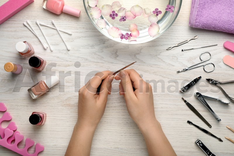 Woman filling nail at white wooden table, top view. Manicure procedure