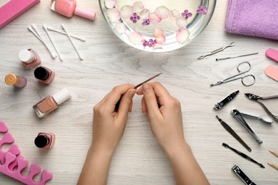 Photo of Woman filling nail at white wooden table, top view. Manicure procedure